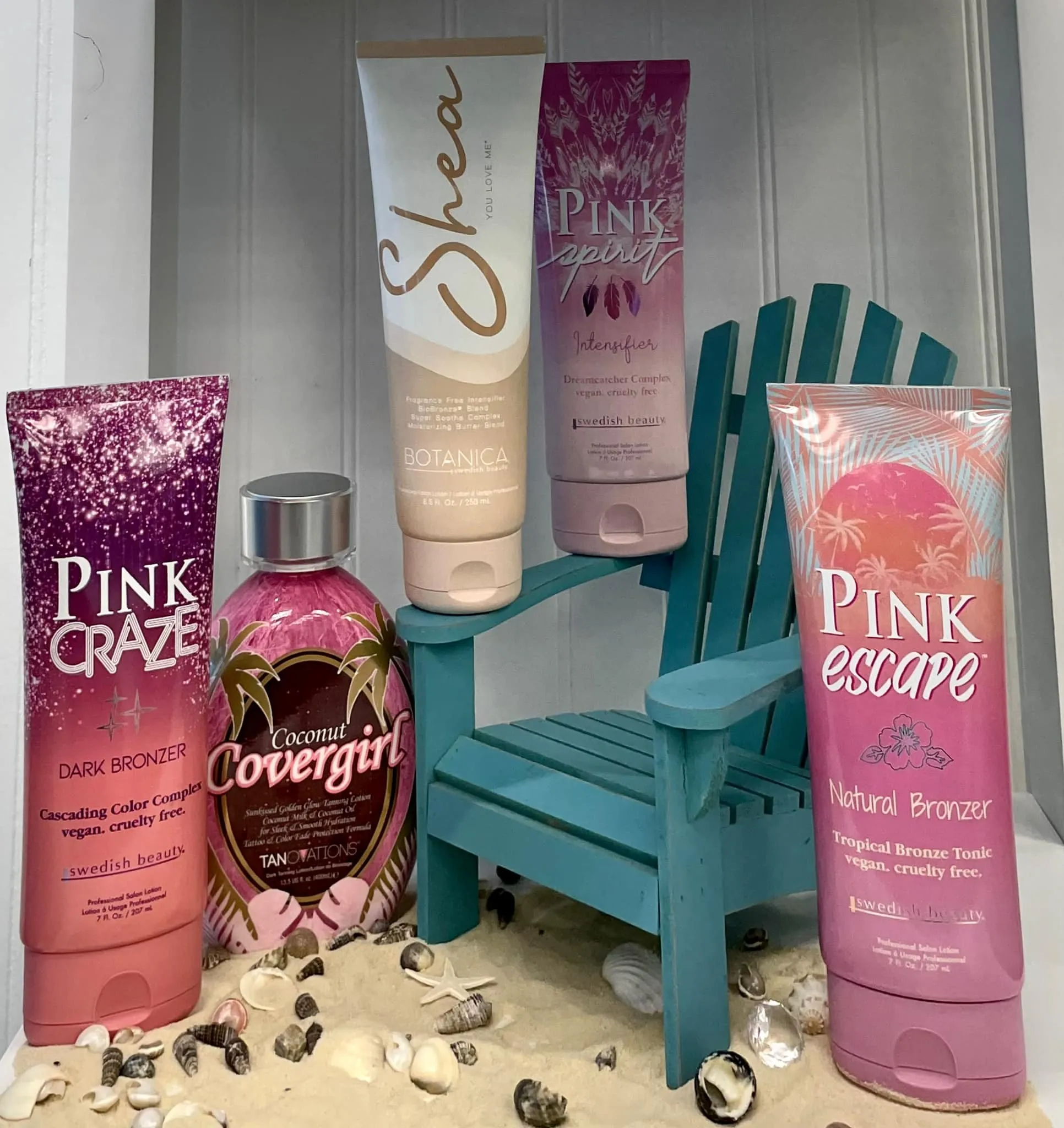 Tanning lotions arranged around a little teal beach chair in sand and shells